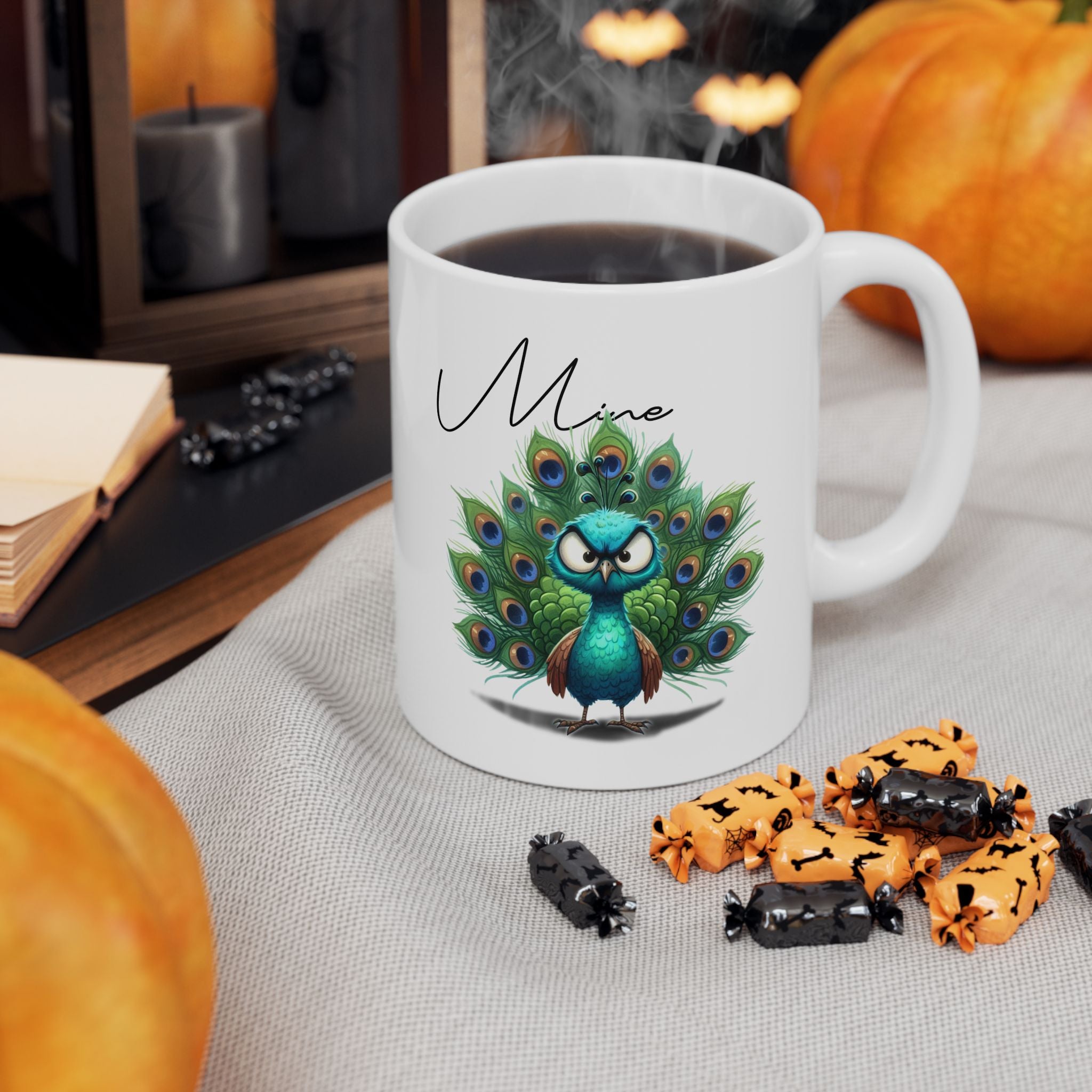 White mug with peacock design and 'Mine' text, surrounded by Halloween-themed treats and pumpkins.