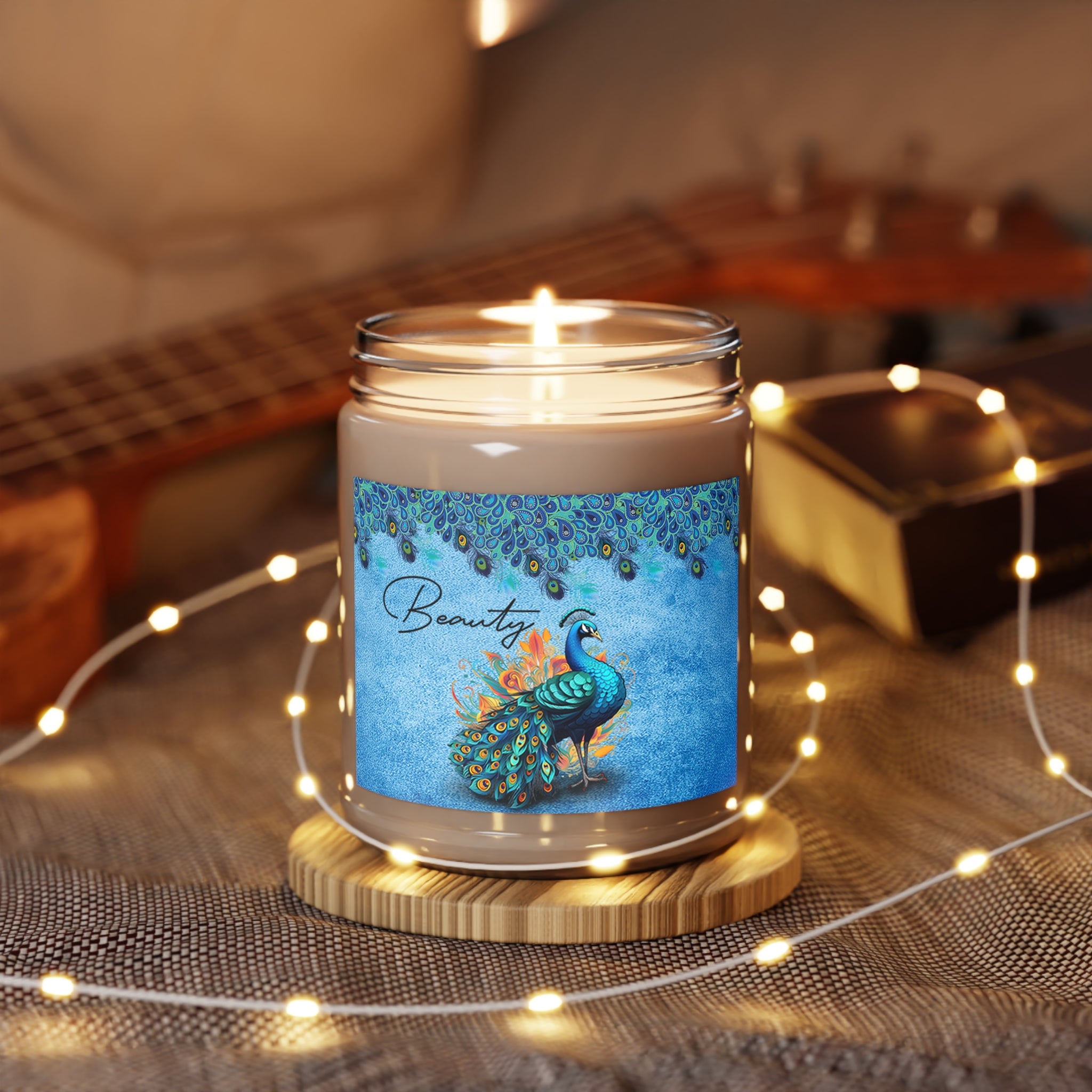 Candle with a peacock design label on a wooden coaster, surrounded by string lights and a guitar in the background.