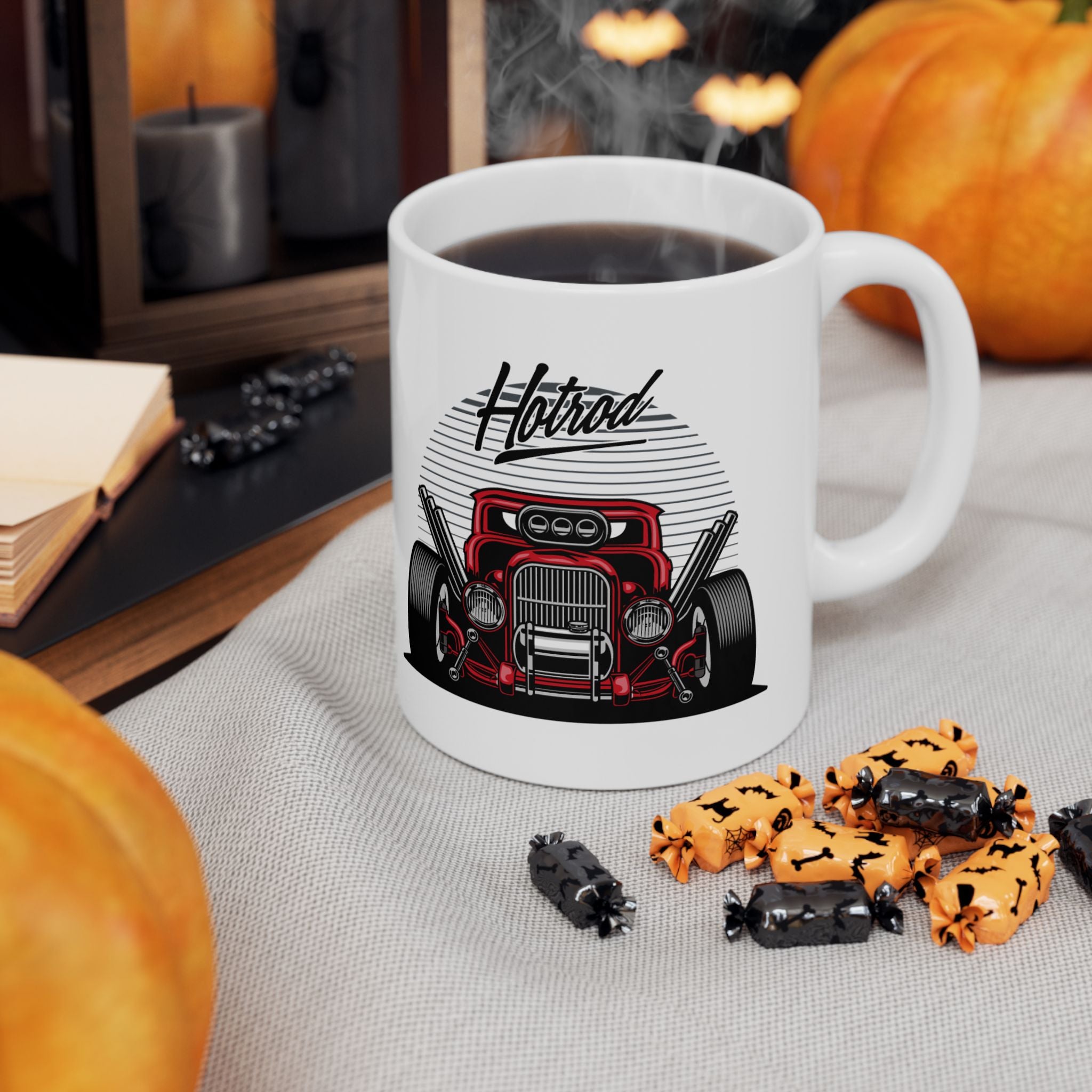 White mug with car design and 'Hotrod' text, filled with coffee, on a table with pumpkins and Halloween-themed treats.