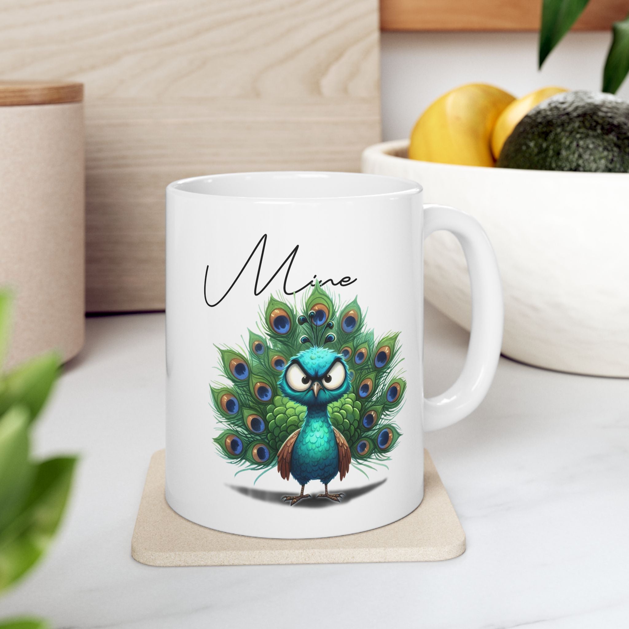 White mug with a peacock design and 'Mine' text on a wooden coaster.