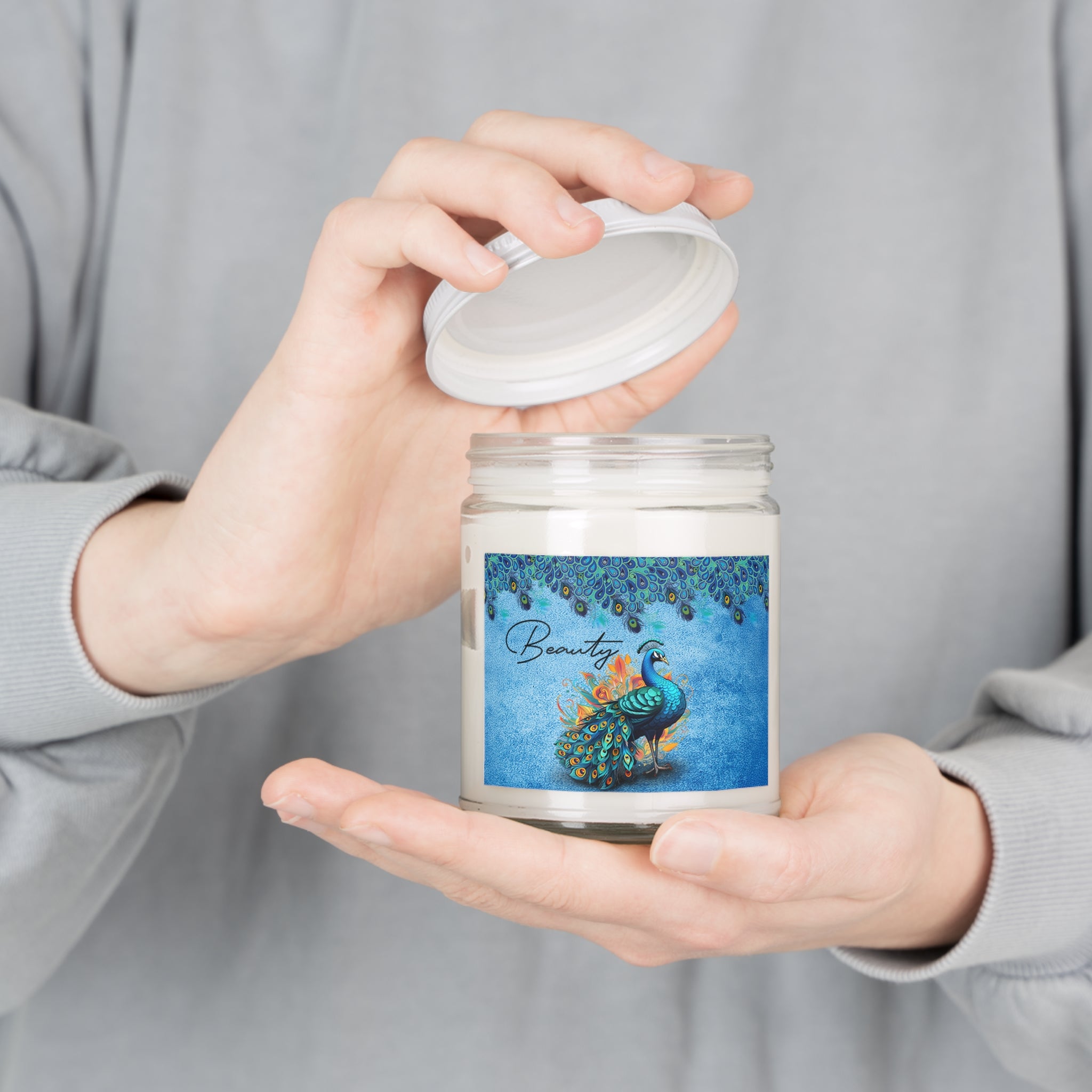 Person holding a candle jar with a decorative label featuring a peacock.