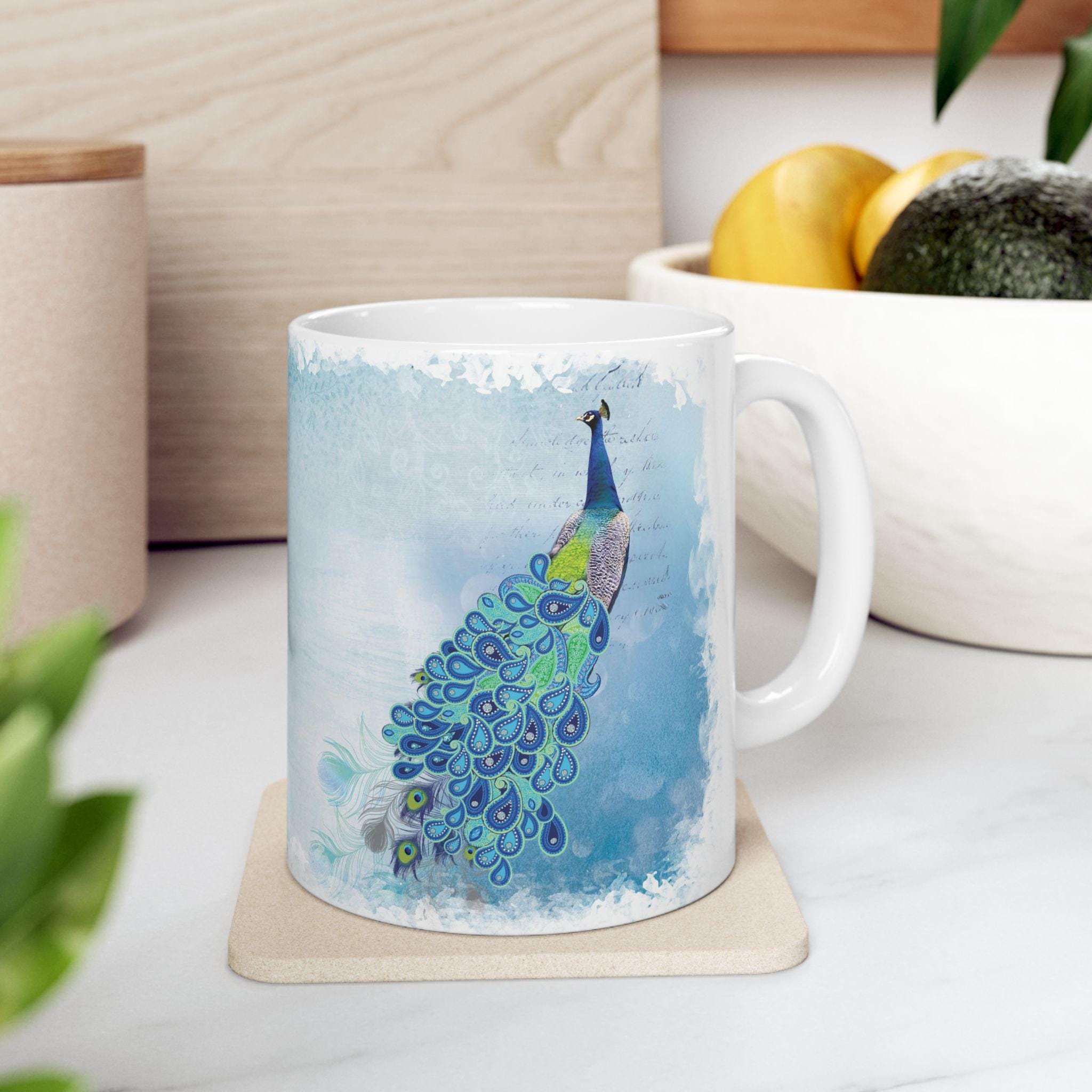 Mug with a peacock design on a coaster, surrounded by plants and a bowl of fruit.