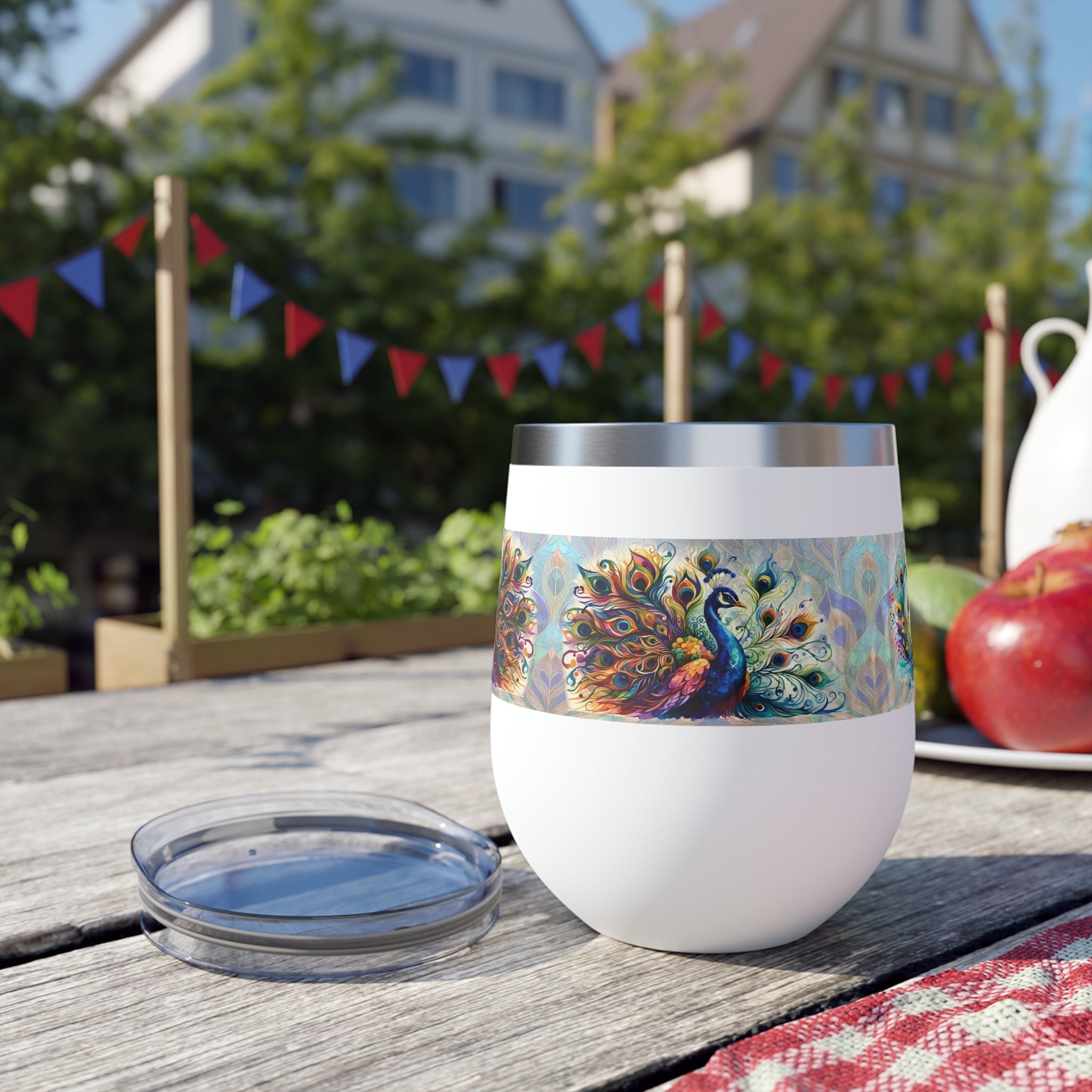 White wine tumbler with peacock design on a wooden table outdoors