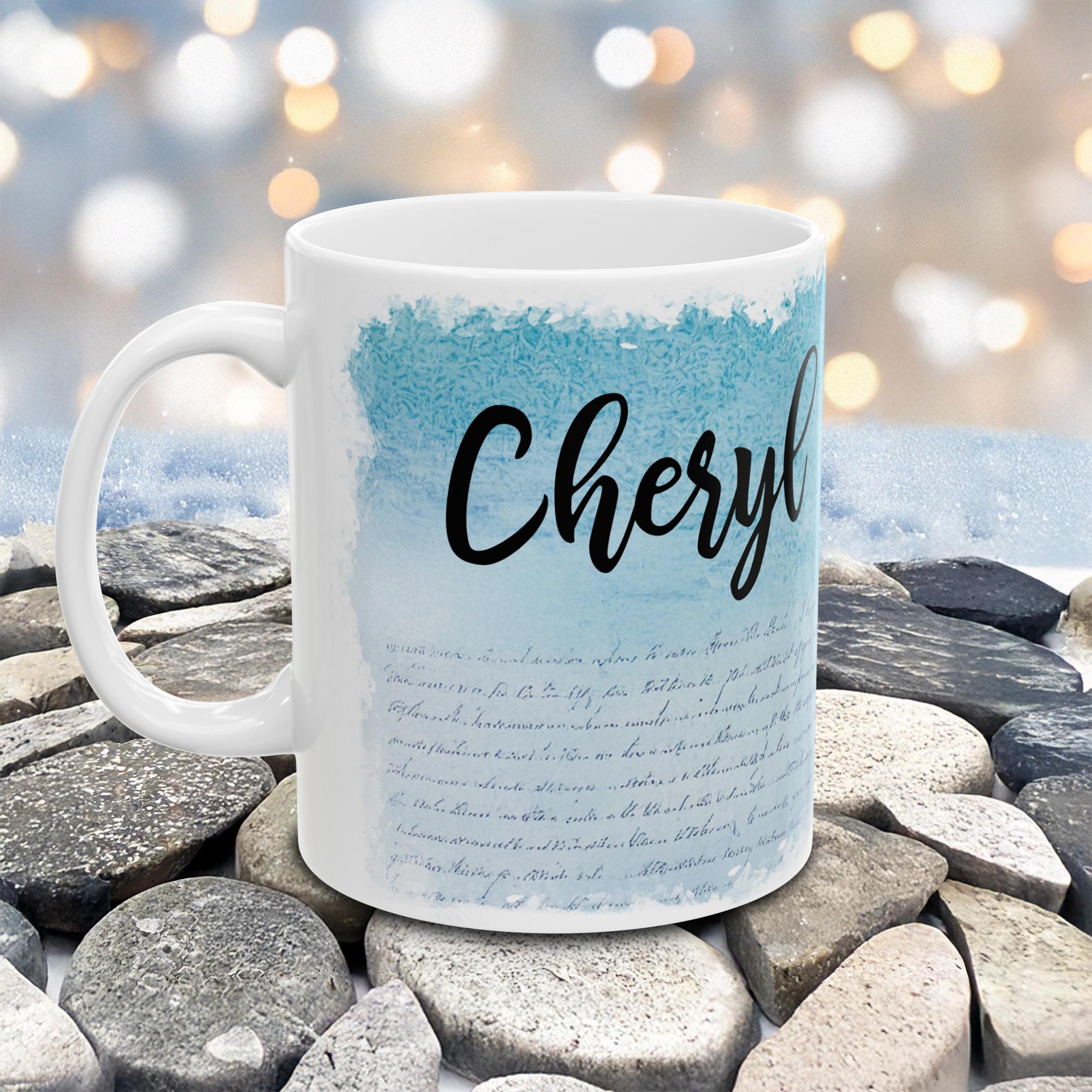 White mug with 'Cheryl' printed on it, placed on stones with a blurred natural background