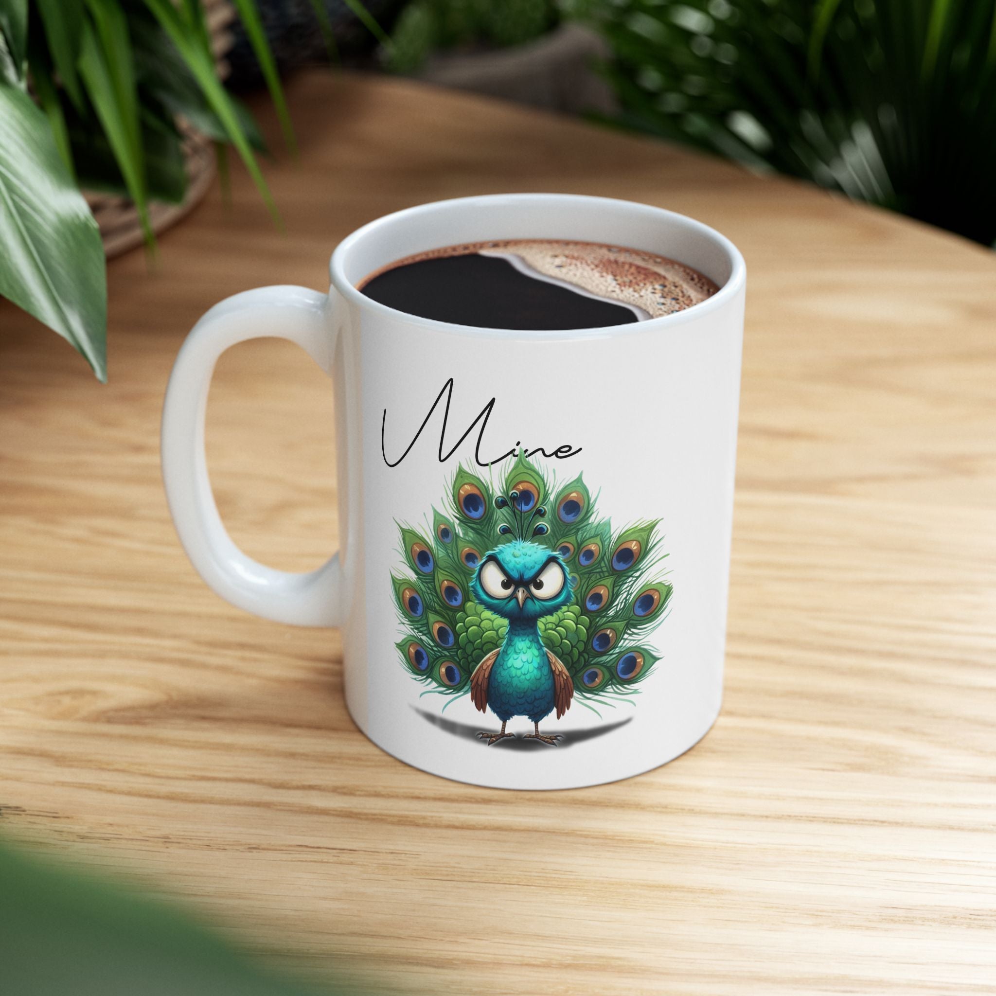 White mug with a peacock design and 'Mine' text on a wooden surface.