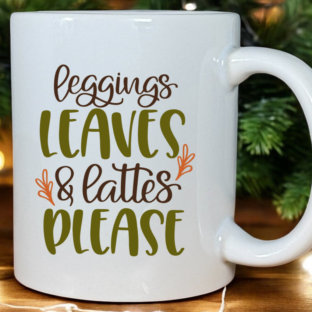 White mug with text 'Leggings, Leaves & Lattes Please' on a wooden surface with Christmas decorations.