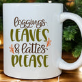 White mug with text 'Leggings, Leaves & Lattes Please' on a wooden surface with Christmas decorations.