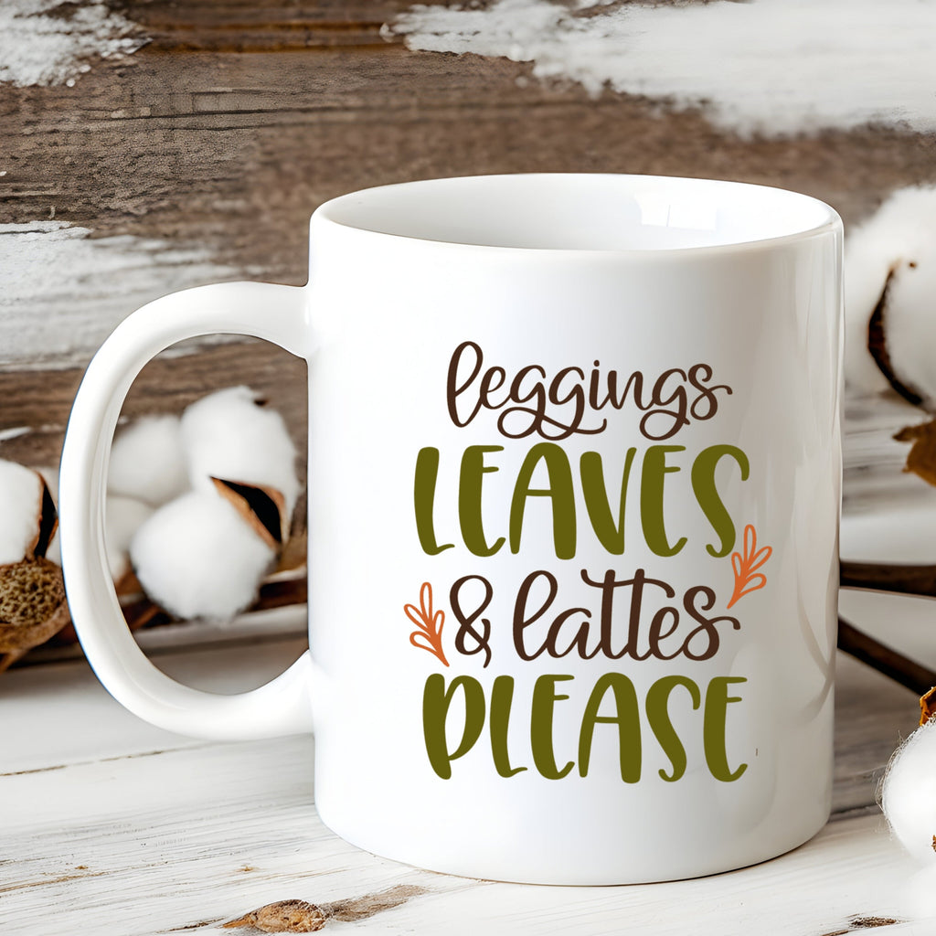 White mug with 'Leggings Leaves & Lattes Please' text on a wooden surface with cotton branches.