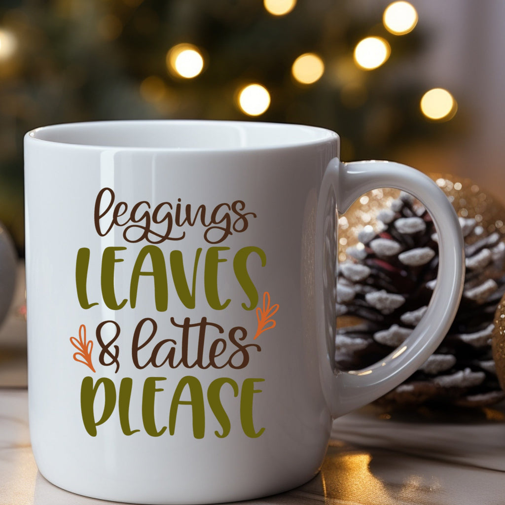 White mug with 'Leggings Leaves & Lattes Please' text against a festive background with lights and pinecones.