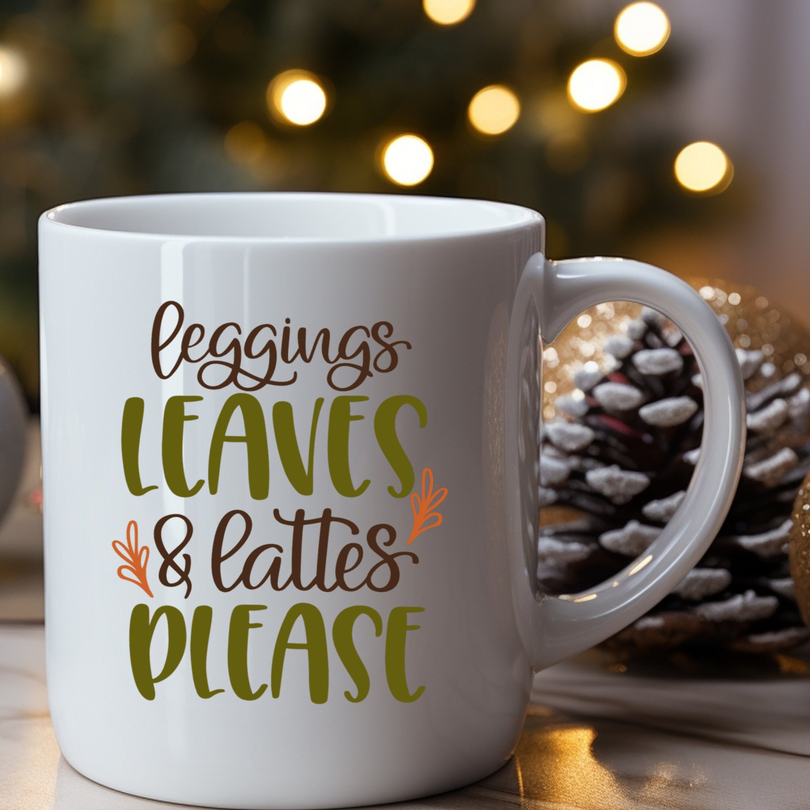 White mug with 'Leggings Leaves & Lattes Please' text against a festive background with lights and pinecones.