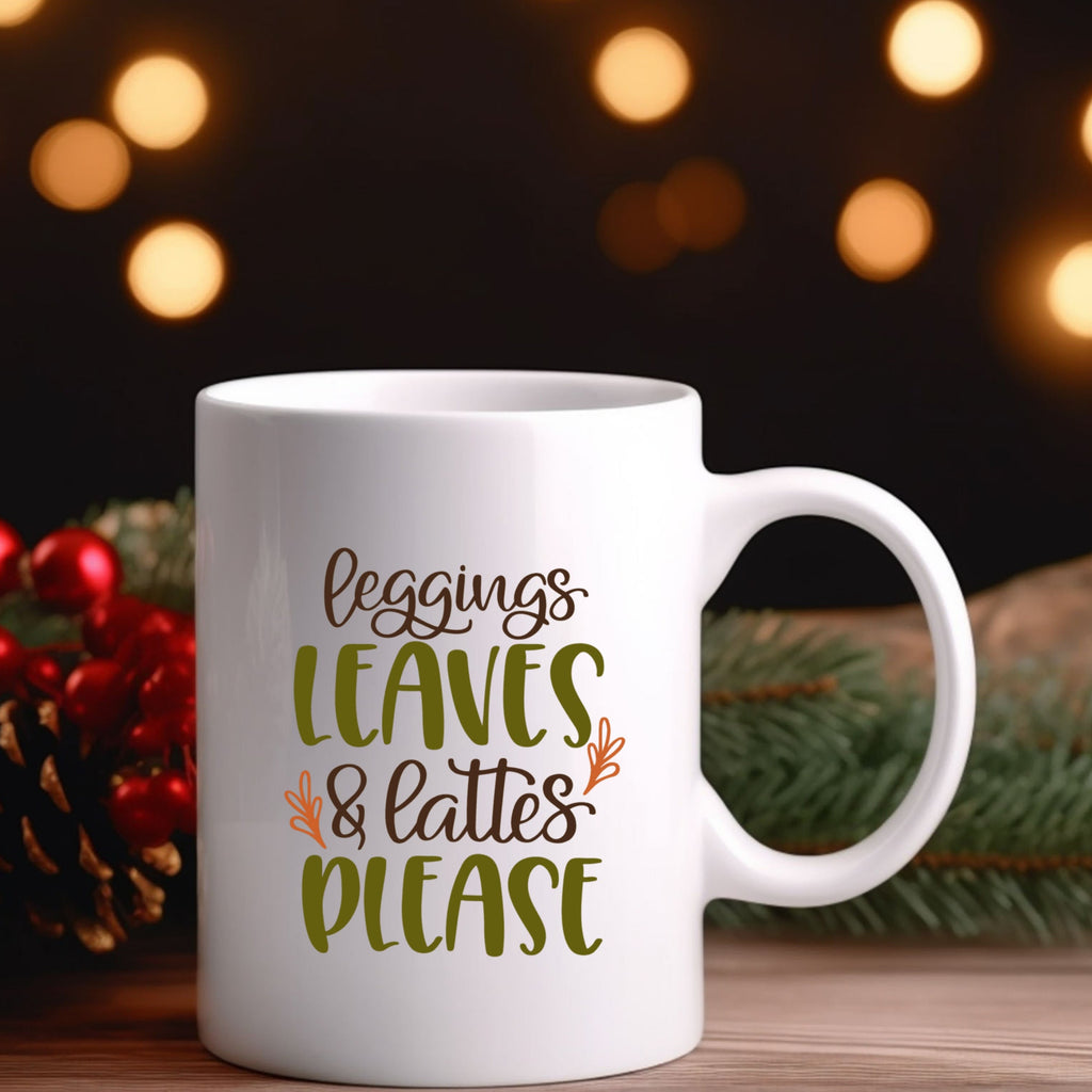 White mug with text 'leggings leaves & lattes please' on a festive background with lights and pine cones.
