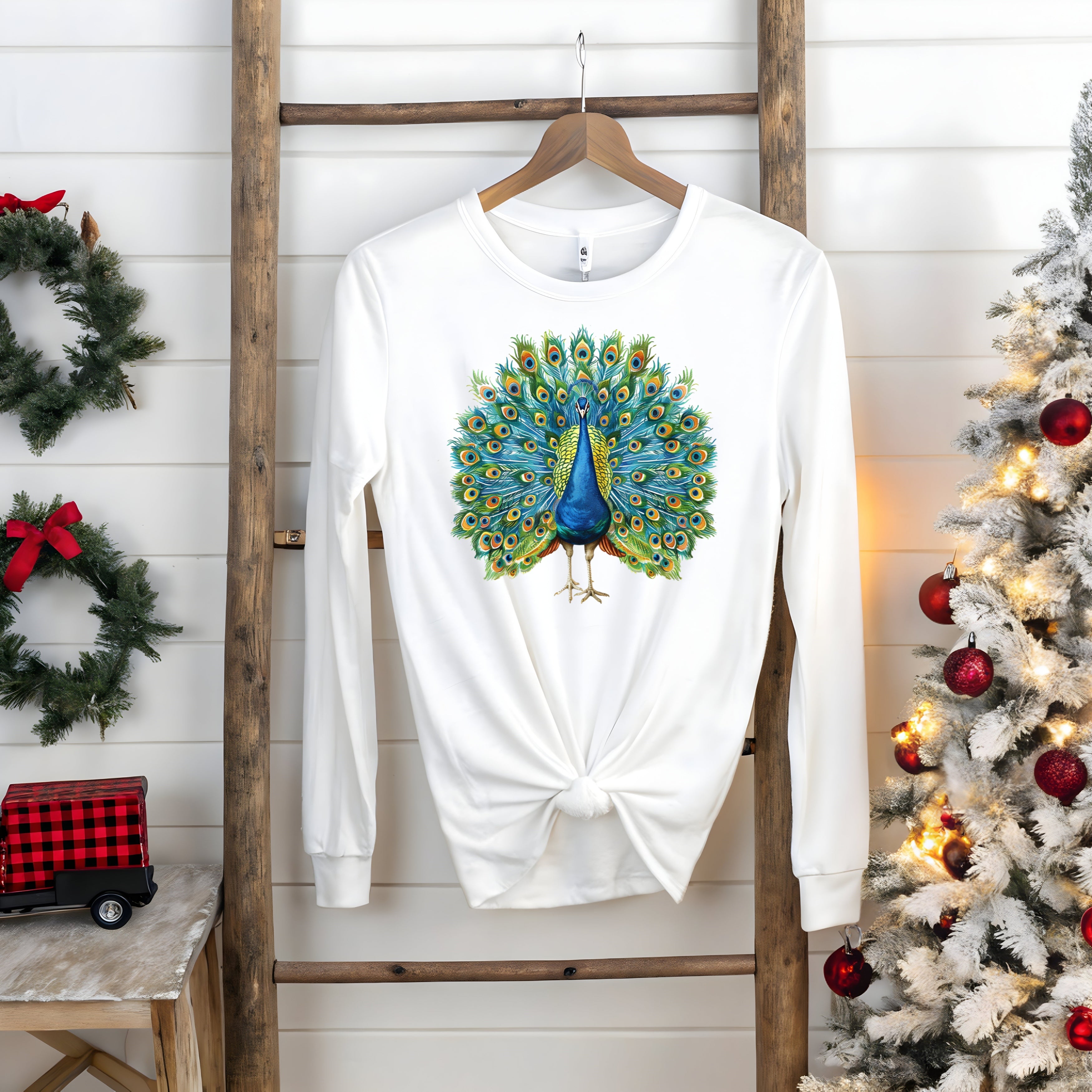 White long-sleeve tee with vibrant peacock design on a wooden hanger, part of a Bella Canvas collection.