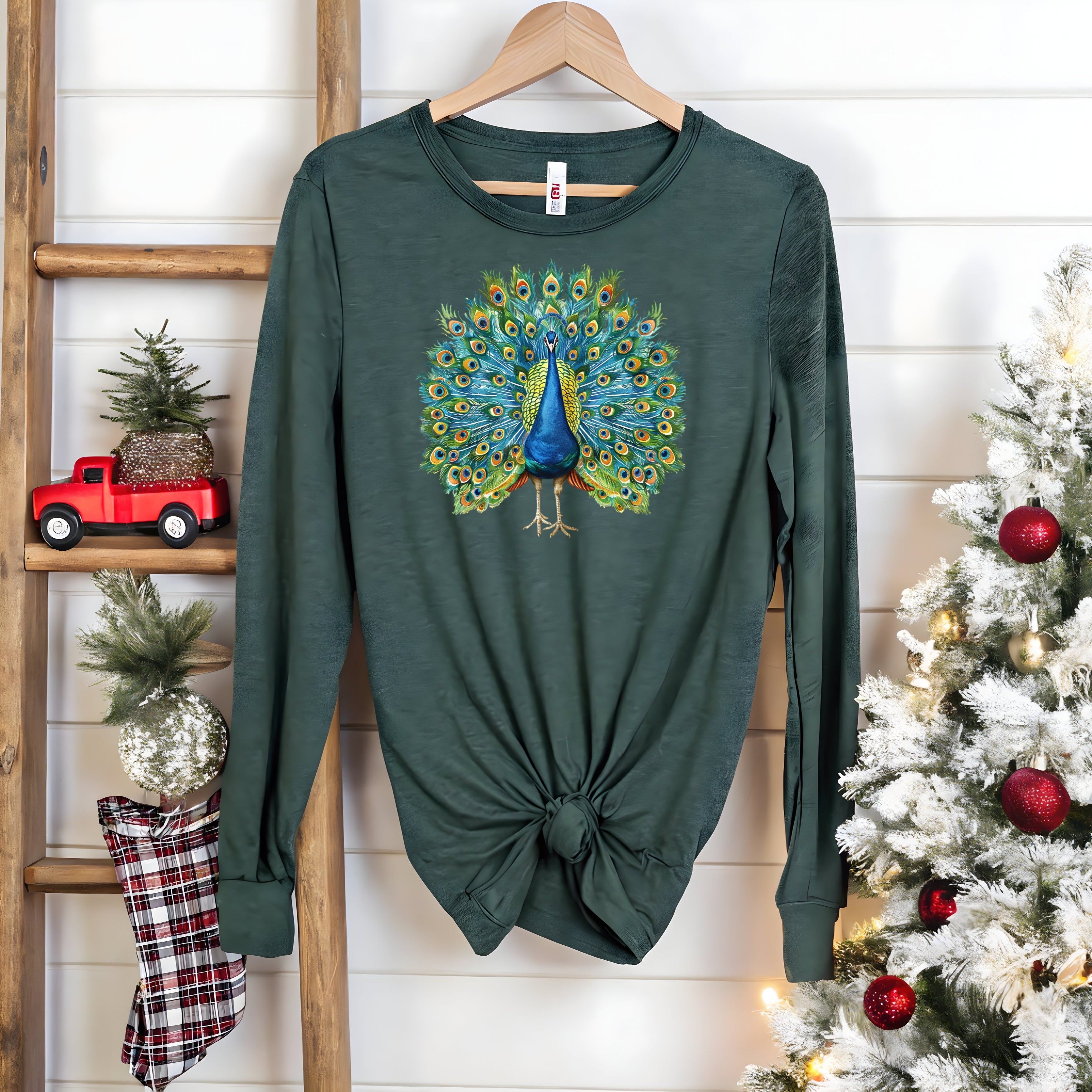 Unisex long-sleeve tee with vibrant peacock graphic, dark green color, knotted at the waist, Bella Canvas brand.