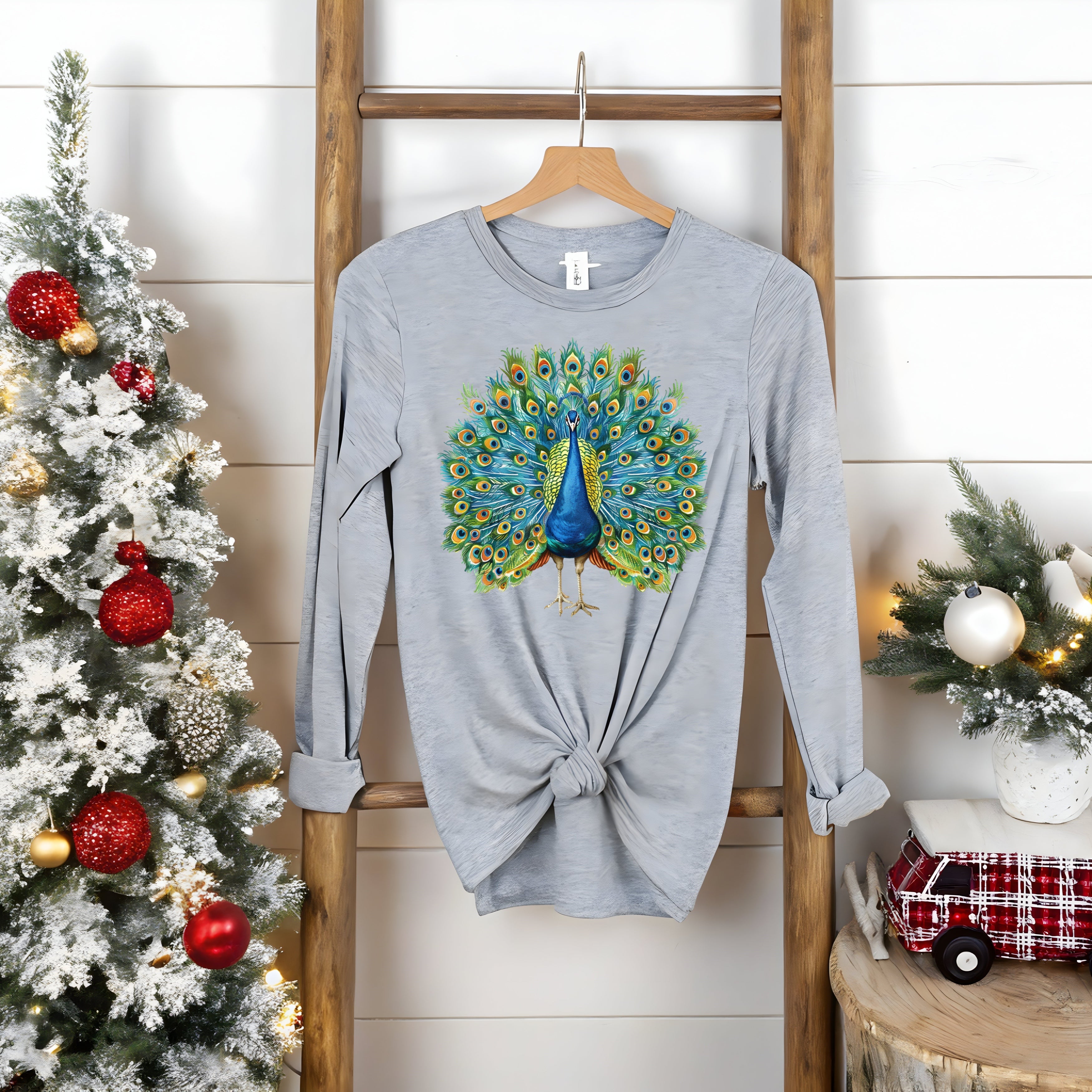 Gray Bella Canvas long-sleeve tee with vibrant peacock design, knotted at waist, on wooden ladder. Nature art long sleeve.
