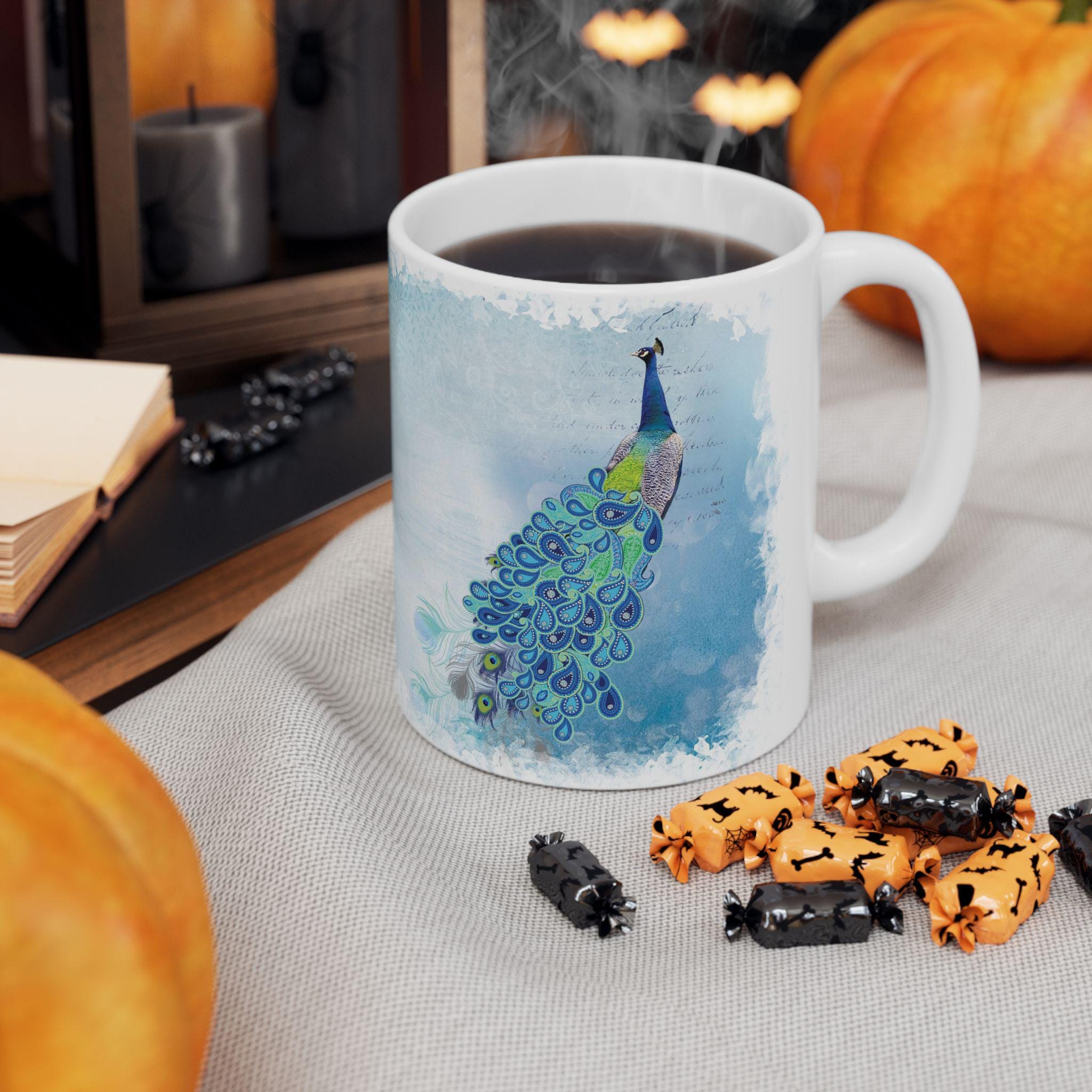Mug with peacock design on a table with pumpkins and Halloween-themed treats.