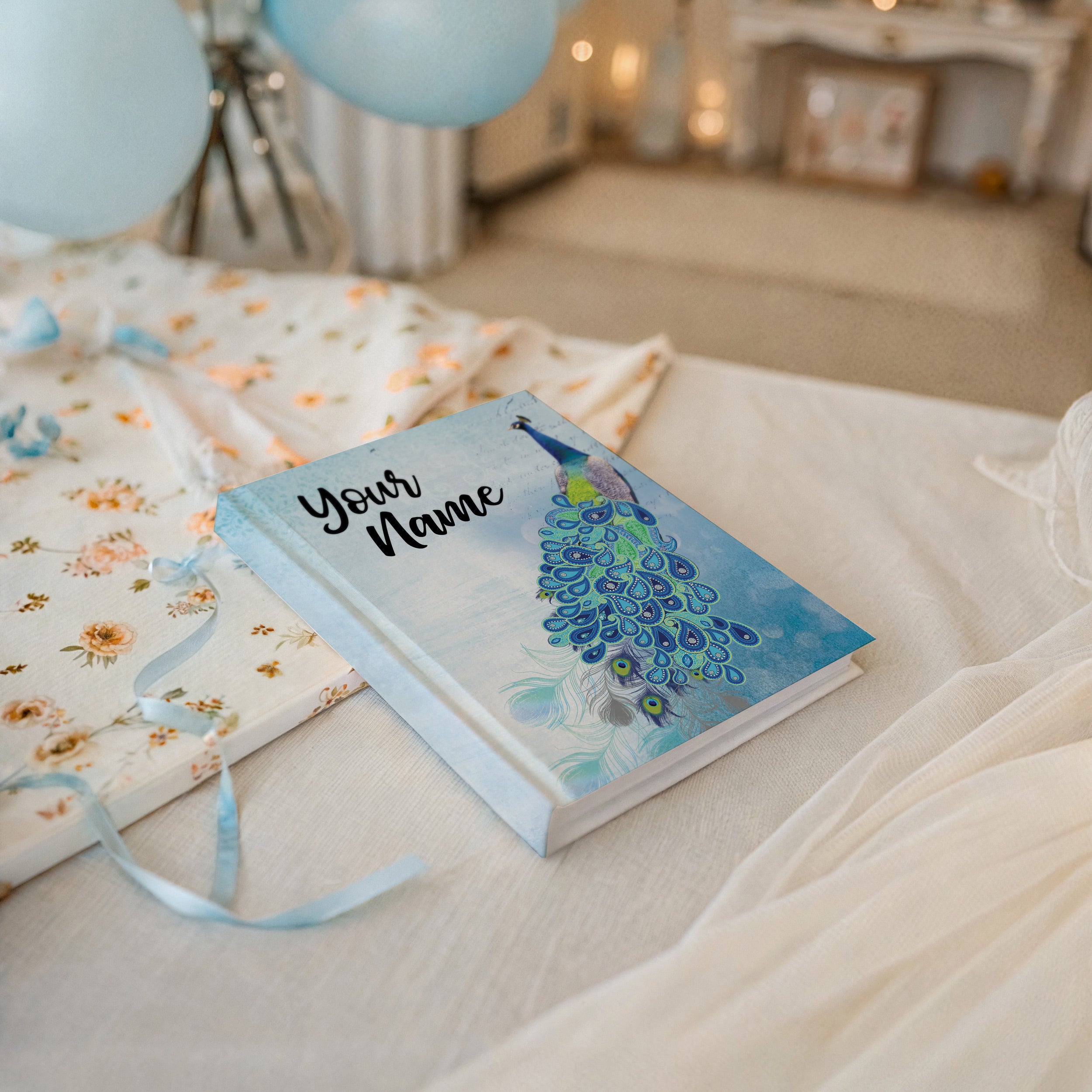 Book with peacock design and 'Your Name' text on a bed with balloons in the background