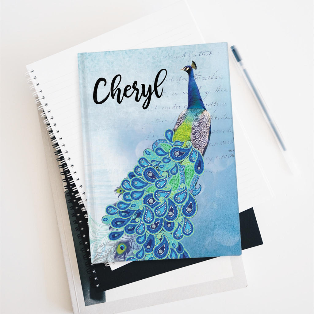 Personalized peacock journal with blue bird design and name, blue cover, on stacked notebooks with a pen.